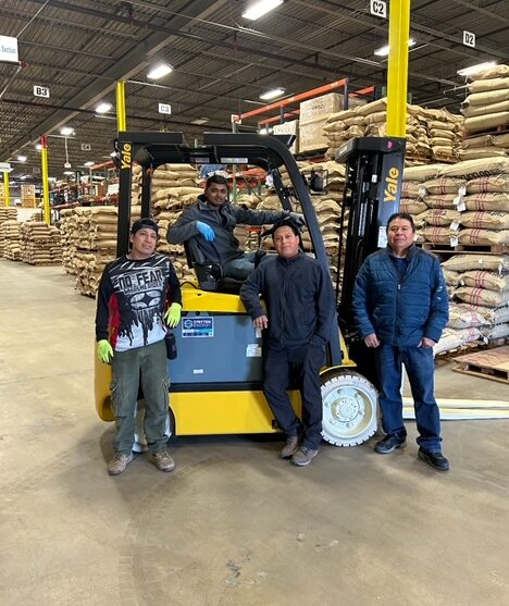 Four workers posing around a forklift and smiling at the camera.