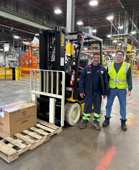 Two workers standing next to a Yale forklift and smiling at the camera.